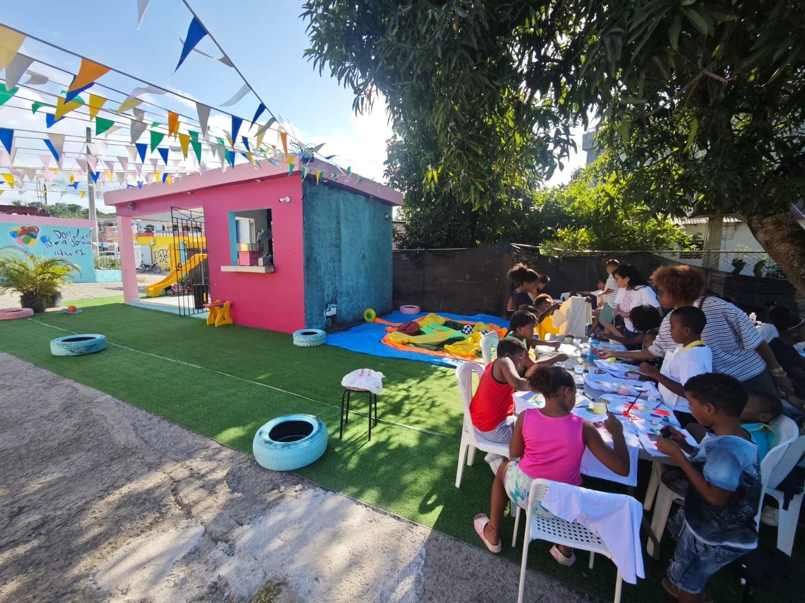 El parque principal de Dulce Vida: casita rosada, grama, banderines y mesas bajo los árboles